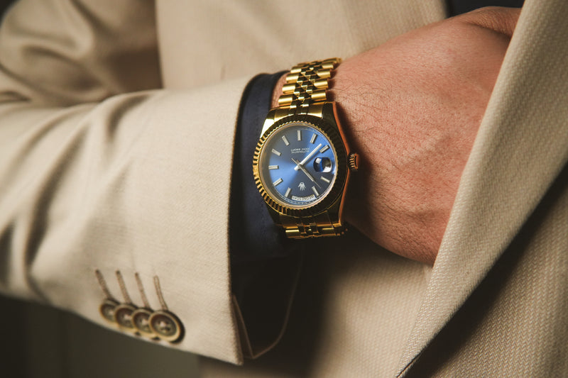 Gold wristwatch on a person wearing a beige suit with a blurred background
