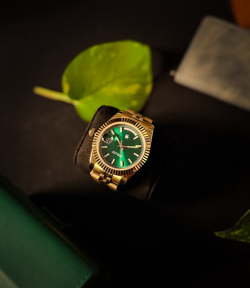 Gold watch with green face on a dark surface with leaves