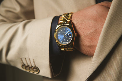 Gold wristwatch on a person wearing a beige suit with a blurred background