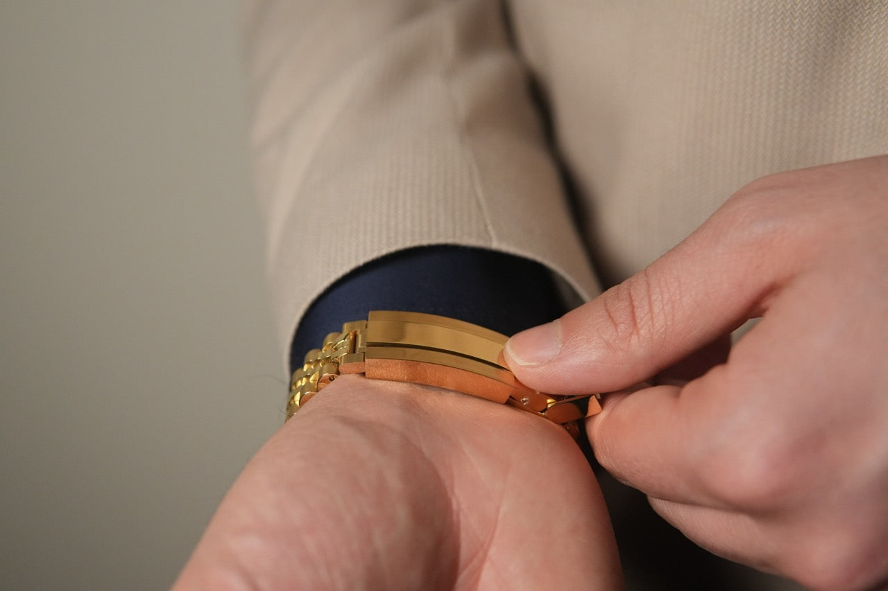 Close-up of hands adjusting a gold bracelet on a neutral background