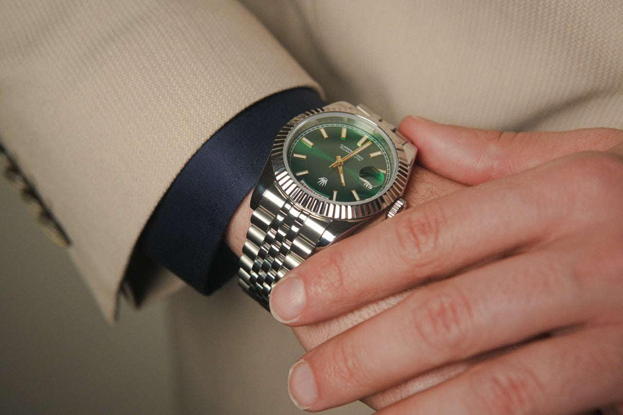 Close-up of the Valenne left-handed watch worn on the right wrist with a beige jacket, showing the green dial.