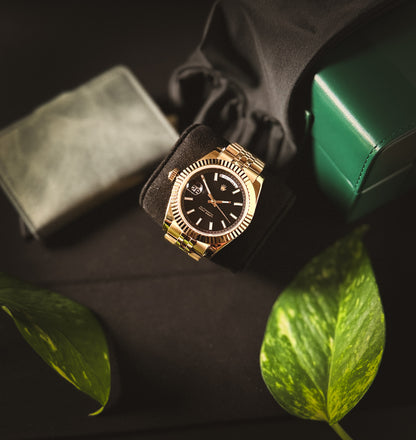 Macro lifestyle shot of the Valenne Destro watch showcasing the black sunburst dial and gold-tone hands with tones of green on the background